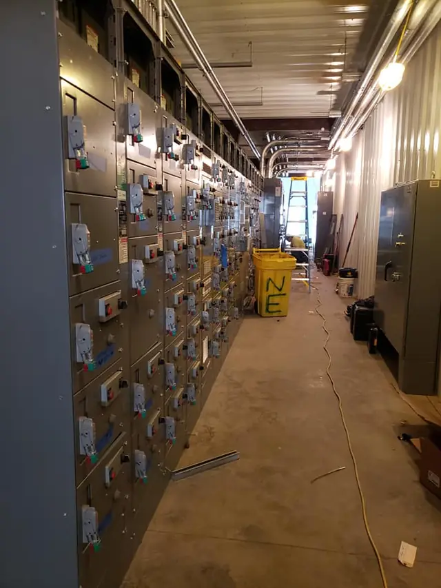 An industrial switchgear room wired by Nuechterlein Electric, a bucket on the floor hand lettered NE.